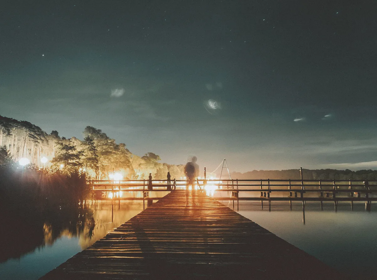 Fotografia nocna — pomost nad jeziorem, światła i gwiazdy, Jakub Klisowski JVISION